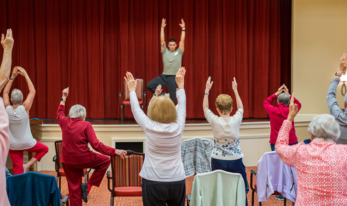 Seniors taking a chair fitness class with an instructor on the stage